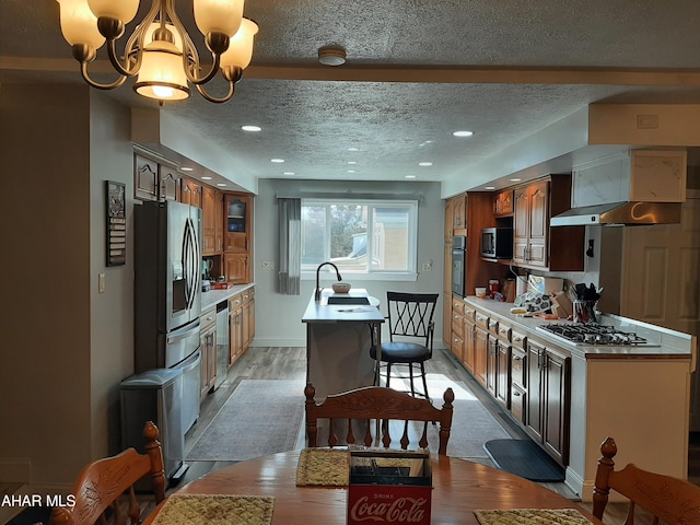 kitchen with appliances with stainless steel finishes, wall chimney exhaust hood, a textured ceiling, light hardwood / wood-style flooring, and a chandelier