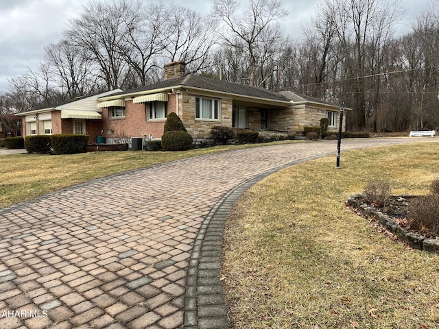 view of front facade featuring decorative driveway, brick siding, a chimney, stone siding, and a front lawn