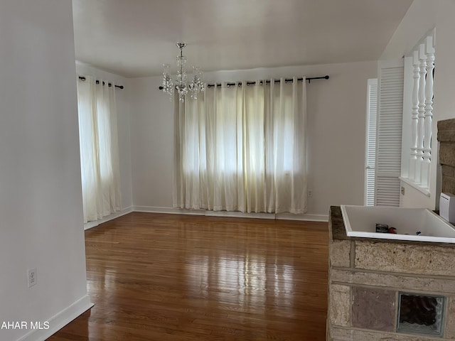 unfurnished dining area featuring baseboards, plenty of natural light, wood finished floors, and a notable chandelier