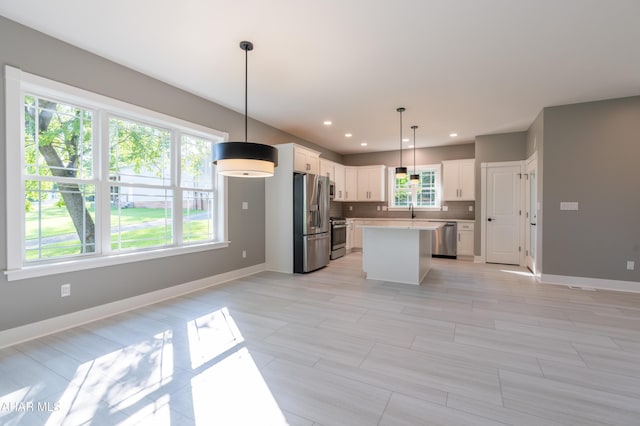 kitchen featuring appliances with stainless steel finishes, backsplash, pendant lighting, a center island, and white cabinetry