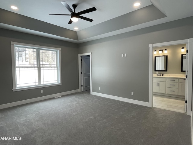 unfurnished bedroom featuring ceiling fan, a raised ceiling, sink, and ensuite bath