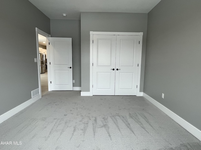 unfurnished bedroom featuring stainless steel fridge with ice dispenser, a closet, and light colored carpet