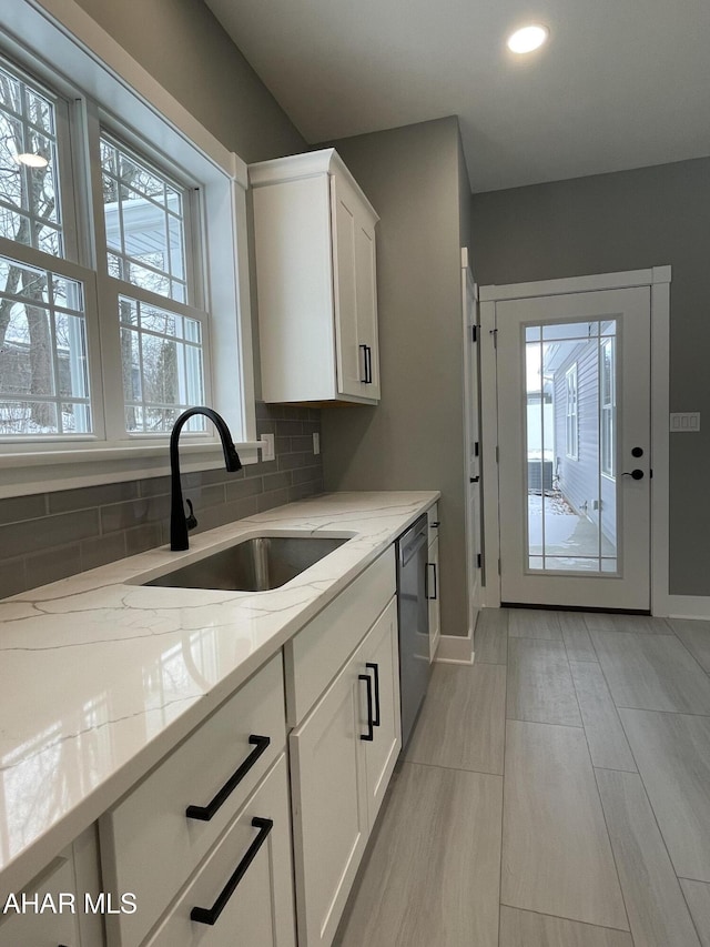 kitchen with light stone countertops, tasteful backsplash, sink, dishwasher, and white cabinetry