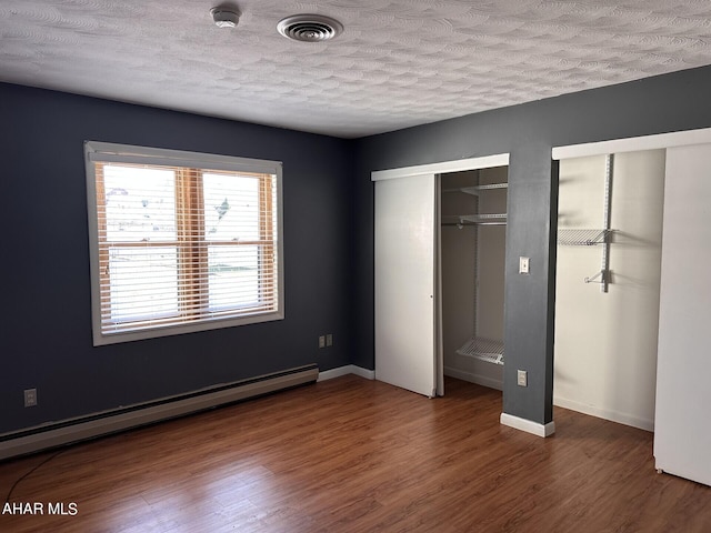 unfurnished bedroom featuring dark hardwood / wood-style flooring, a textured ceiling, and a baseboard heating unit