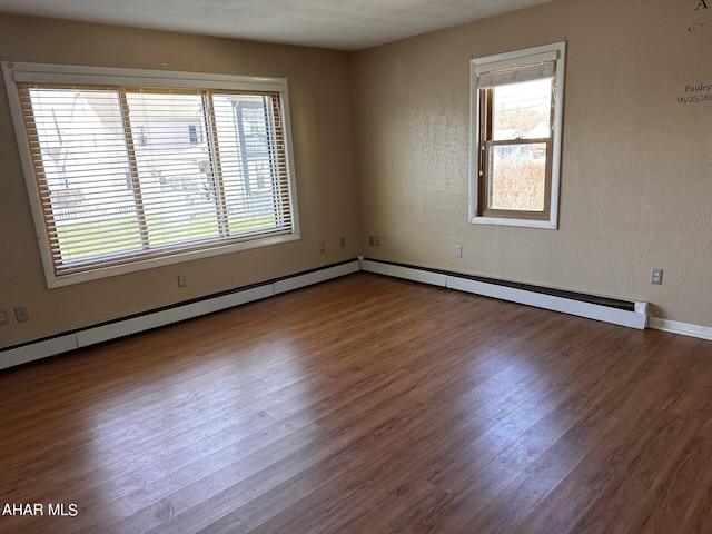 empty room with hardwood / wood-style floors, a healthy amount of sunlight, and a baseboard heating unit