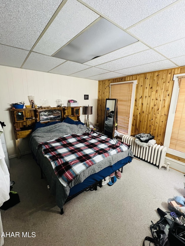 bedroom featuring wooden walls, carpet flooring, and a drop ceiling