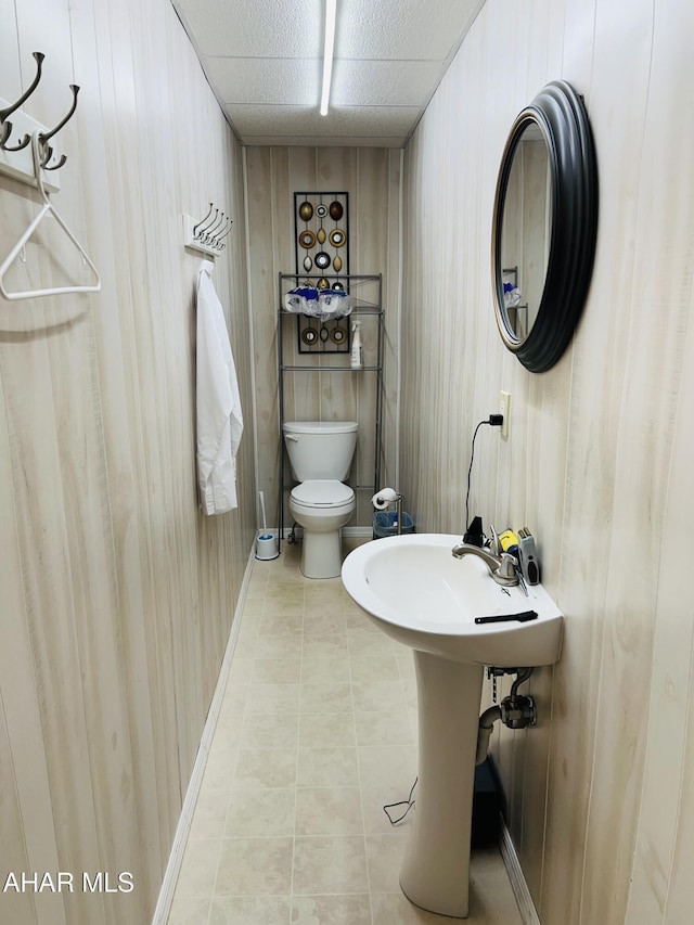 bathroom featuring a paneled ceiling, wood walls, sink, toilet, and tile patterned floors