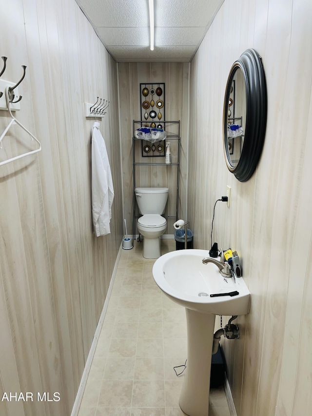 bathroom with tile patterned floors, toilet, and wood walls