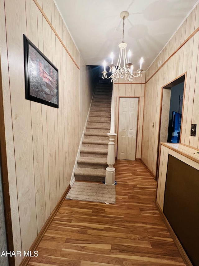 corridor with wood walls, hardwood / wood-style floors, and a notable chandelier