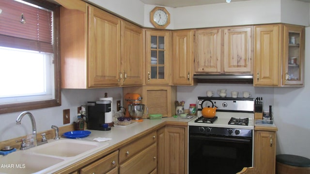 kitchen featuring light countertops, glass insert cabinets, a sink, and gas range