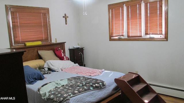 bedroom with a baseboard heating unit and wood finished floors