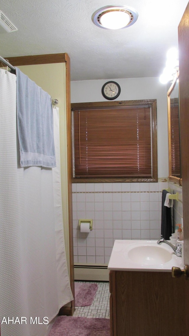 bathroom with visible vents, a baseboard radiator, tile patterned flooring, vanity, and tile walls