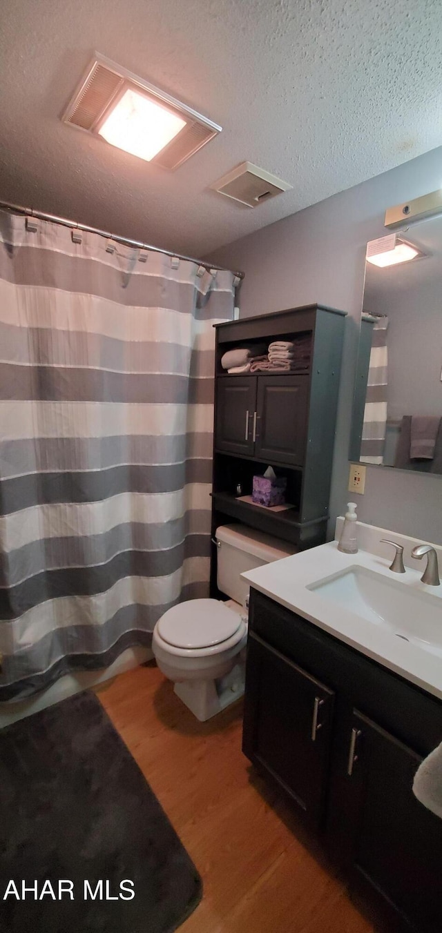 bathroom with a textured ceiling, hardwood / wood-style floors, vanity, and toilet