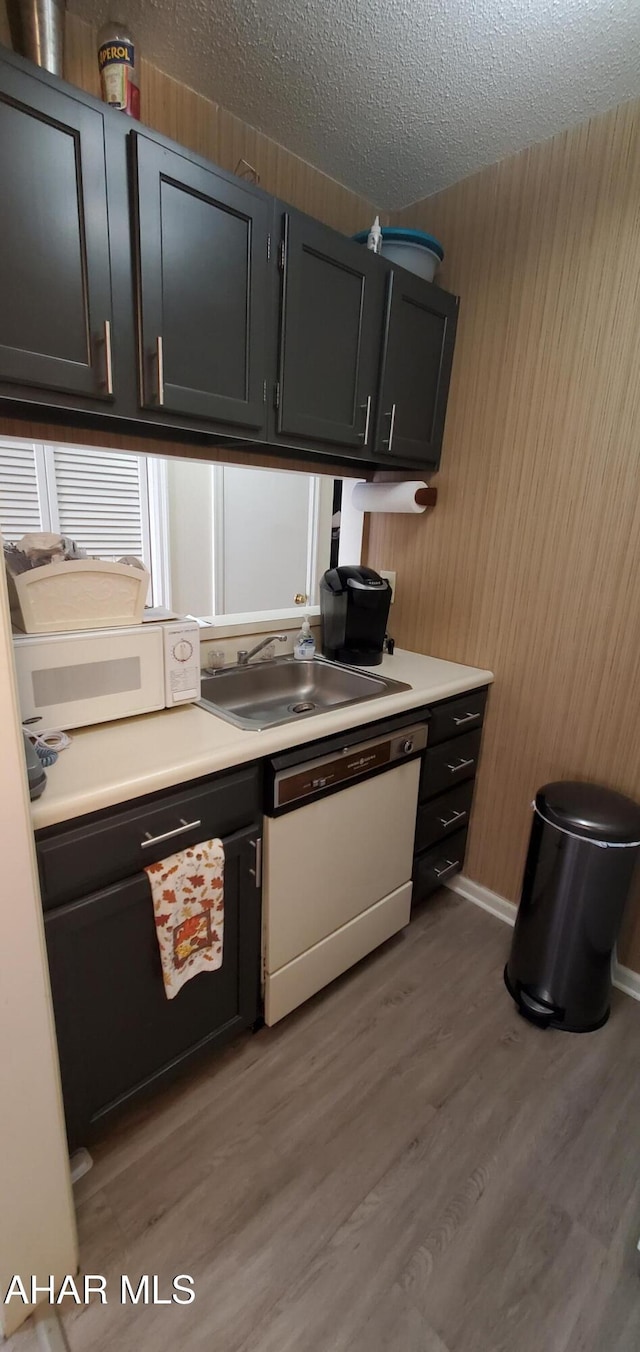 kitchen with white appliances, hardwood / wood-style floors, wooden walls, a textured ceiling, and sink