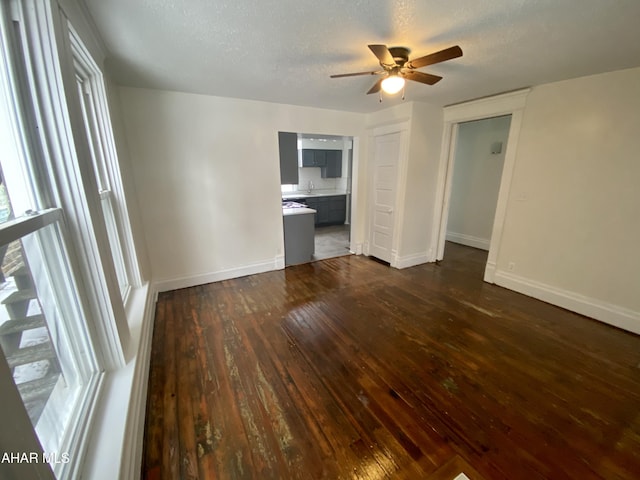 unfurnished room with dark wood finished floors, a ceiling fan, baseboards, a sink, and a textured ceiling