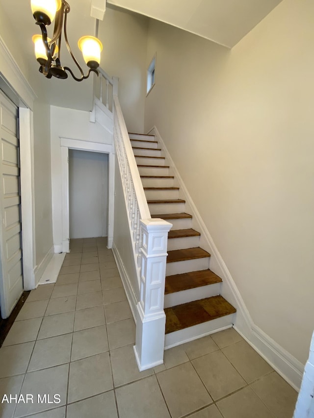 stairway featuring tile patterned floors, a chandelier, and baseboards