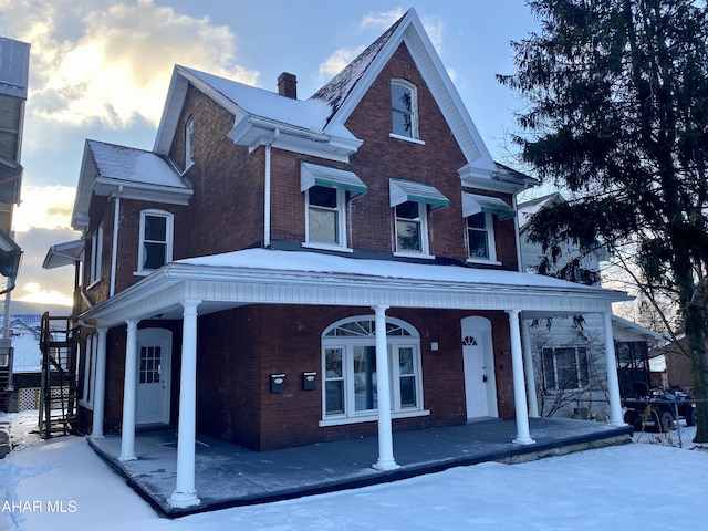 view of front of home with covered porch, brick siding, and a chimney