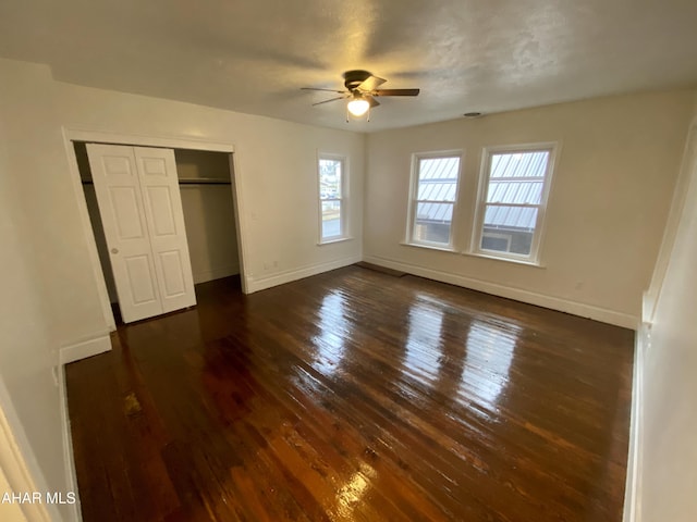 unfurnished bedroom with dark wood-type flooring, baseboards, a closet, and a ceiling fan