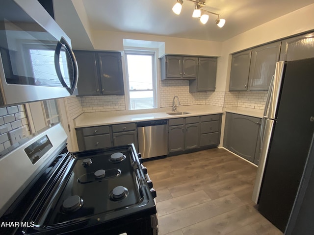 kitchen featuring appliances with stainless steel finishes, gray cabinets, a sink, and tasteful backsplash