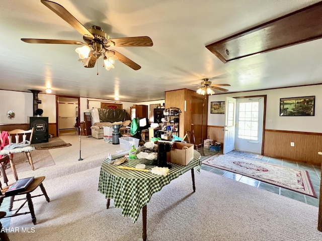 carpeted living room featuring ceiling fan, wood walls, and a wood stove