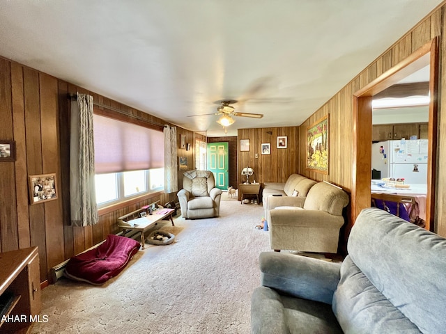 carpeted living room with ceiling fan and wood walls