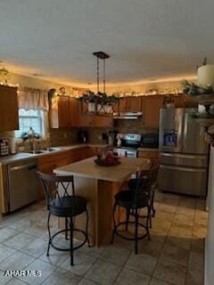 kitchen featuring a kitchen breakfast bar, sink, light tile patterned floors, appliances with stainless steel finishes, and a kitchen island