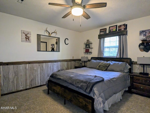 carpeted bedroom featuring wooden walls, ceiling fan, and a textured ceiling