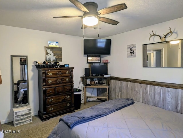 carpeted bedroom featuring ceiling fan, wood walls, and a textured ceiling