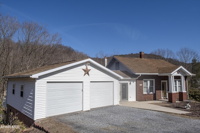 single story home with brick siding, a shingled roof, gravel driveway, a chimney, and an attached garage