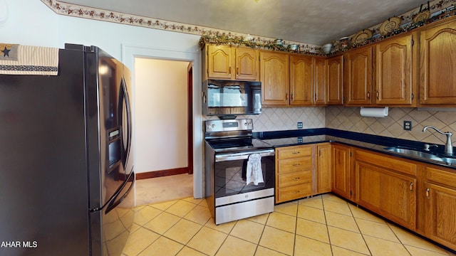 kitchen featuring dark countertops, light tile patterned floors, brown cabinets, black appliances, and a sink