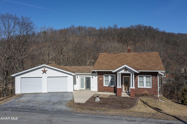 view of front of property with driveway, a shingled roof, a garage, brick siding, and a chimney