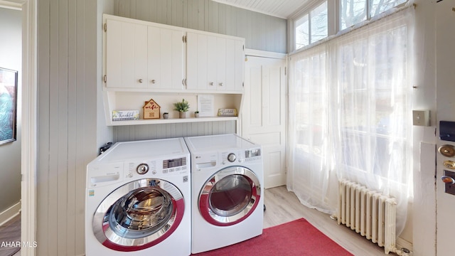 laundry room featuring wood walls, cabinets, washing machine and dryer, light hardwood / wood-style floors, and radiator heating unit