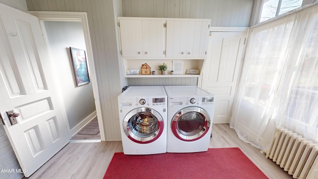 clothes washing area with washing machine and dryer, radiator heating unit, cabinets, and light hardwood / wood-style flooring