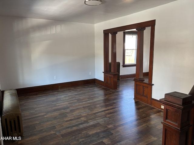 unfurnished room featuring dark hardwood / wood-style flooring, ornate columns, and radiator