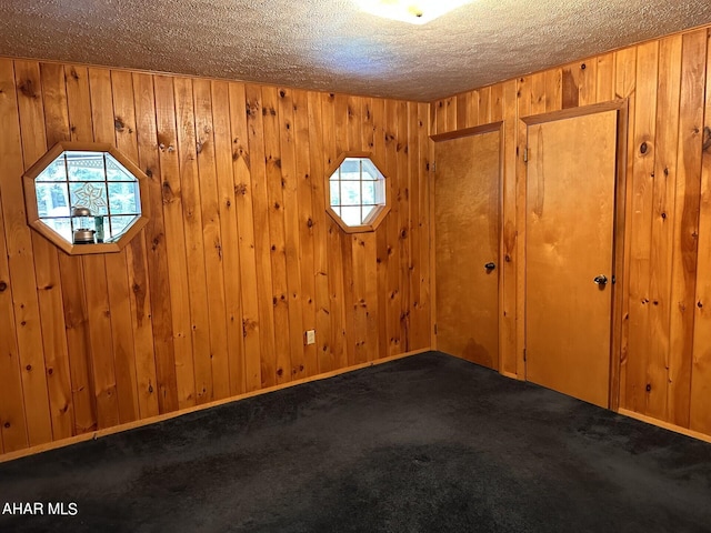 carpeted spare room with wooden walls and a textured ceiling