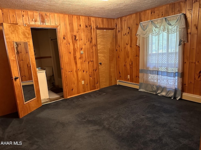 carpeted spare room with wood walls, a baseboard radiator, and a textured ceiling