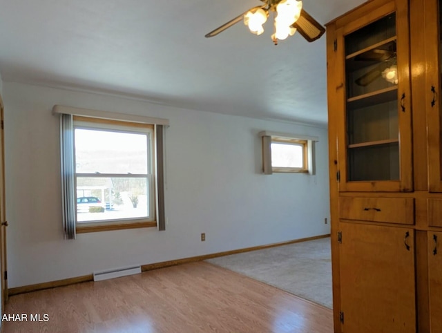 empty room featuring ceiling fan, light hardwood / wood-style flooring, and a baseboard heating unit