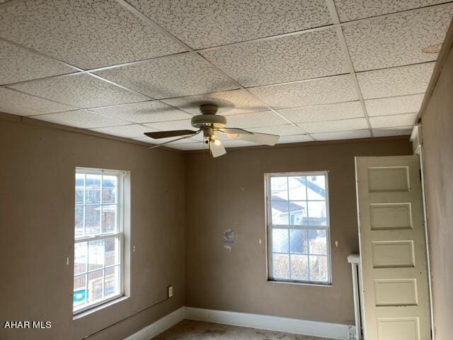 unfurnished room with a paneled ceiling, ceiling fan, and a healthy amount of sunlight