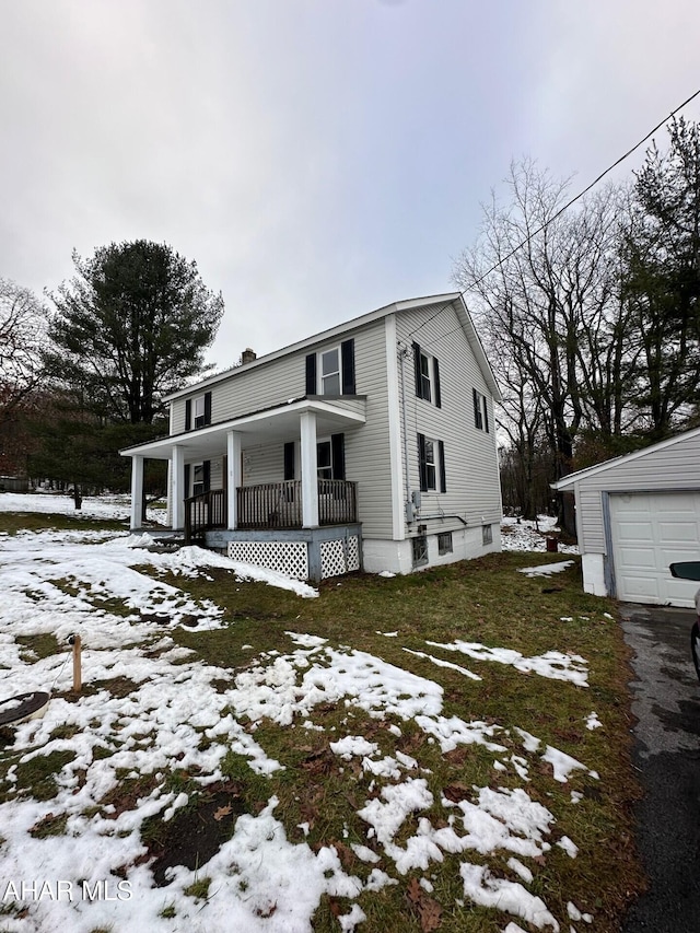 snow covered property featuring a porch, a garage, an outdoor structure, and a yard