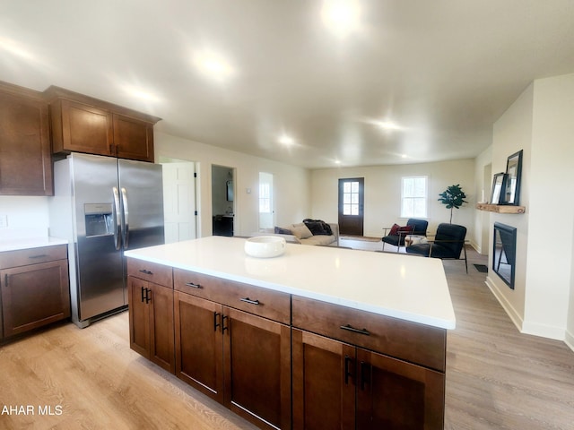 kitchen featuring stainless steel fridge, open floor plan, light wood-style flooring, and a glass covered fireplace