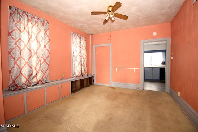 spare room with radiator, light carpet, sink, and ceiling fan