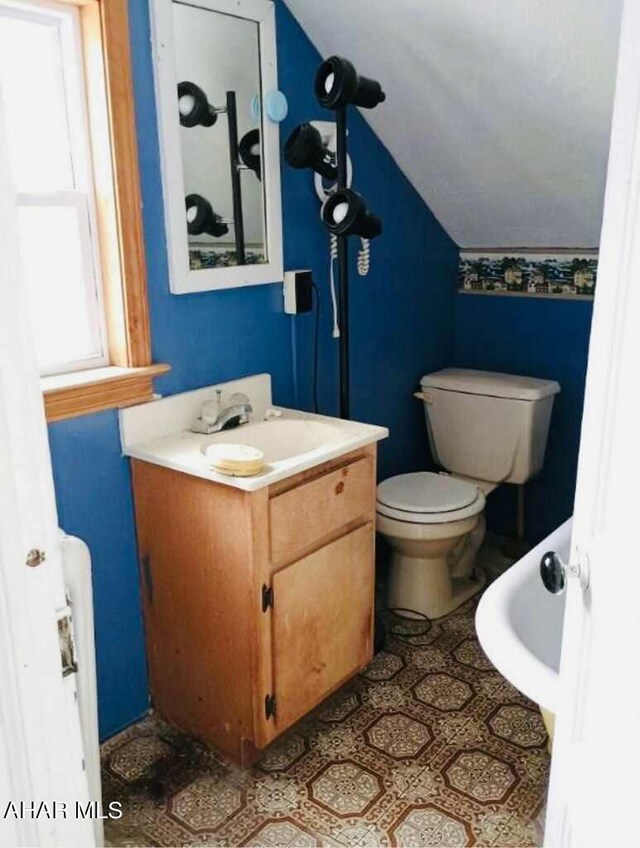 bathroom with toilet, vanity, vaulted ceiling, and a healthy amount of sunlight