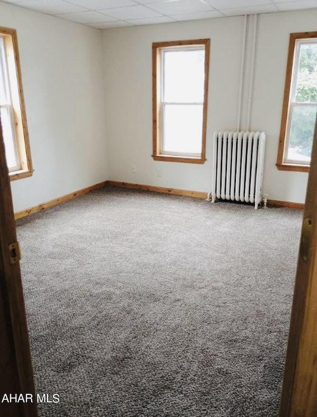 carpeted spare room featuring a paneled ceiling and radiator heating unit