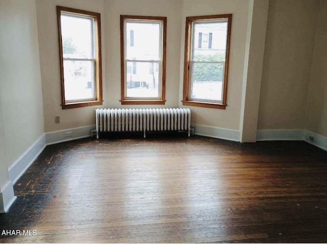 unfurnished room featuring plenty of natural light, radiator, and dark wood-type flooring