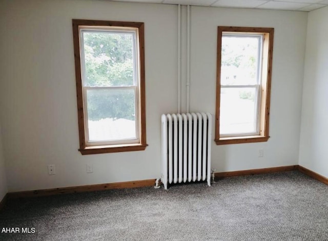 carpeted empty room with radiator, plenty of natural light, and a drop ceiling