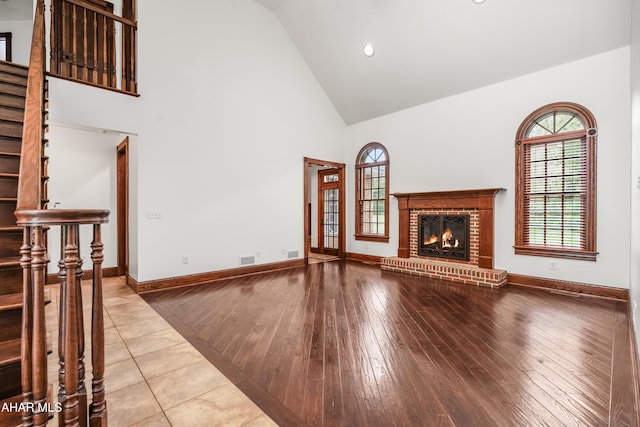 unfurnished living room featuring high vaulted ceiling, light hardwood / wood-style floors, and a brick fireplace