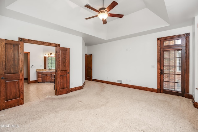 carpeted bedroom featuring a raised ceiling, connected bathroom, and ceiling fan