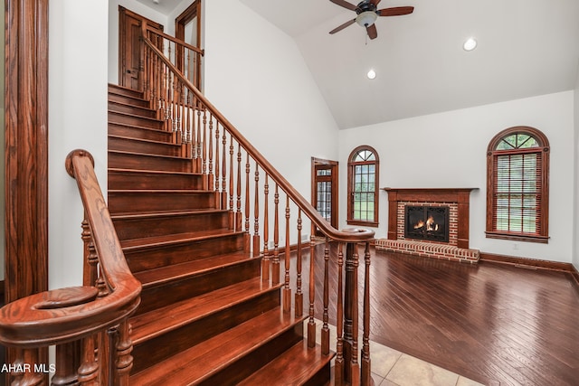 stairway featuring hardwood / wood-style floors, high vaulted ceiling, a brick fireplace, and ceiling fan