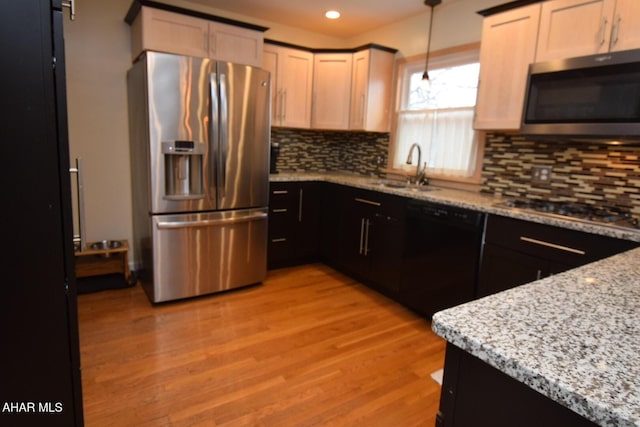 kitchen featuring pendant lighting, sink, stainless steel appliances, light stone counters, and light hardwood / wood-style floors