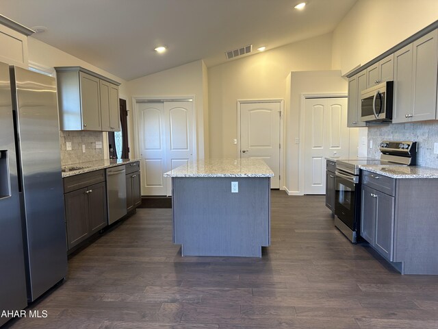 kitchen featuring sink, dark wood-type flooring, stainless steel appliances, light stone counters, and a kitchen island